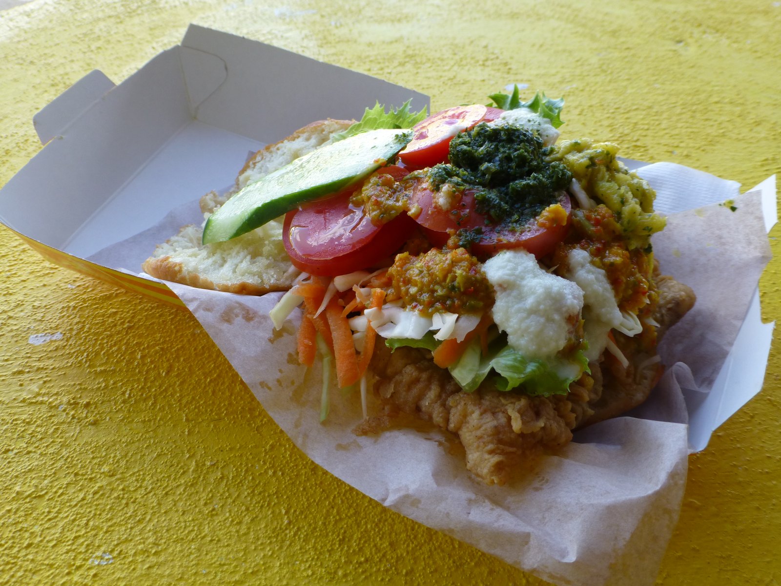 An open bake and shark sandwich topped with cucumber, tomato, shredded vegetables and sauces.